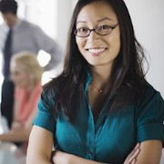 A woman stands with folded arms in front of people at a conference table