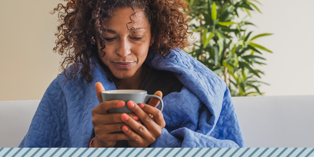 woman wrapped in a blanket, sick, holding a cup of tea